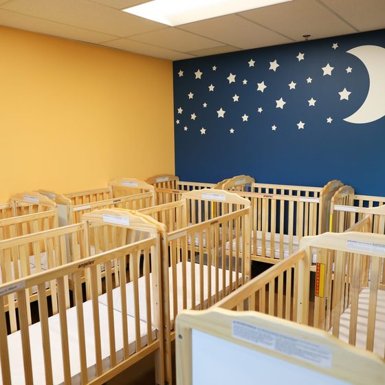 The infant nursery: a row of wooden cribs beneath a moon-and-stars mural