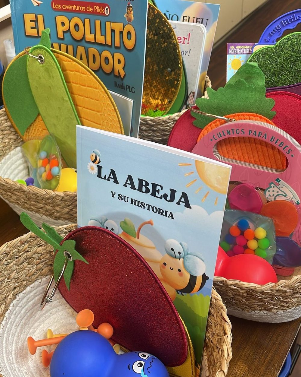 Baskets of Spanish-language children's books and felt sensory toys on a classroom shelf