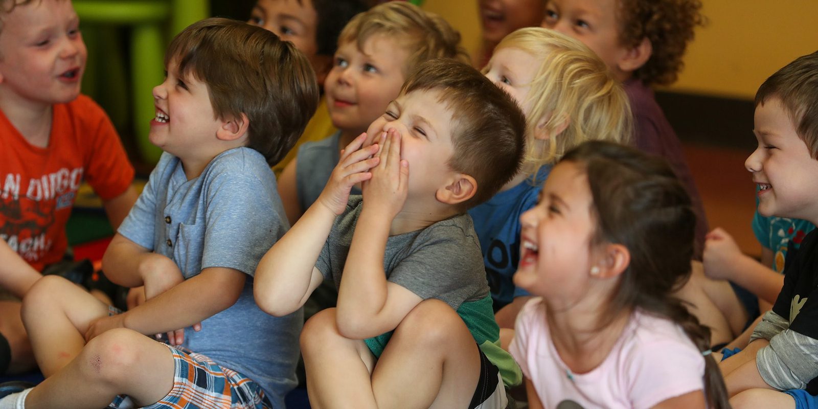 A preschool class sitting cross-legged on the rug, laughing together during story time