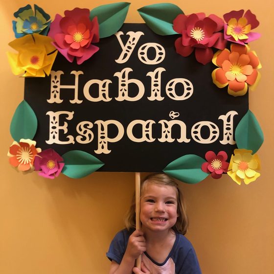 A child holding a paper-flower-framed sign reading Yo Hablo Español