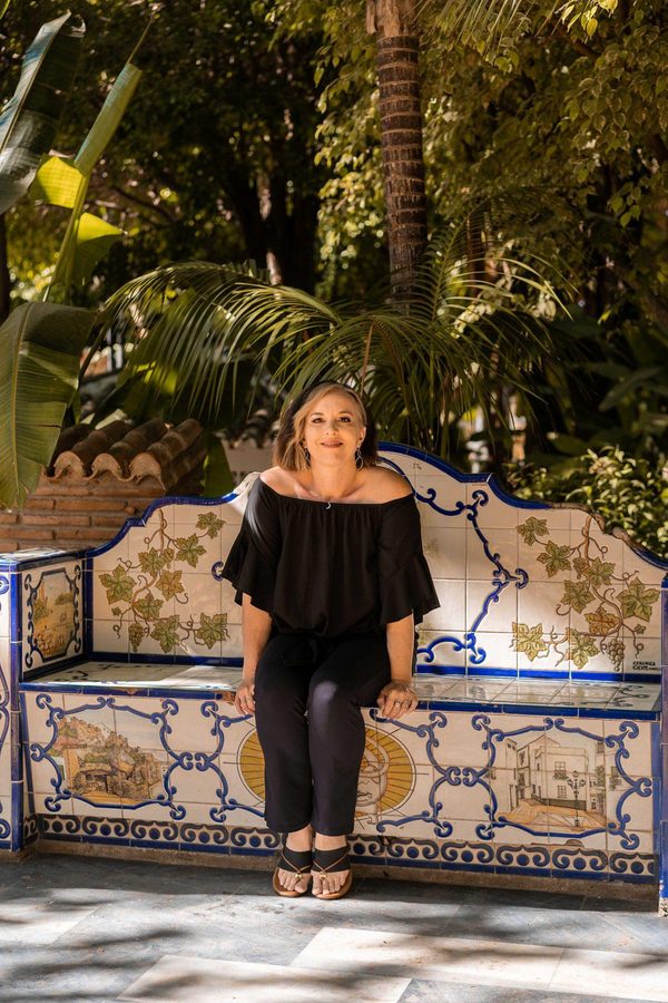 Leah Retamozo seated on a hand-painted tiled bench under palms