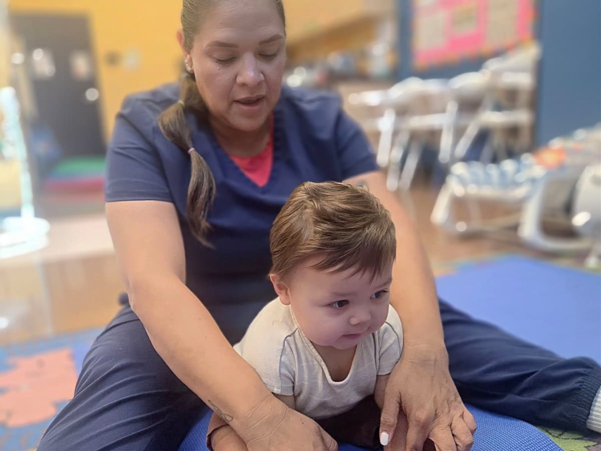 A teacher guiding an infant through a stretch on a yoga mat