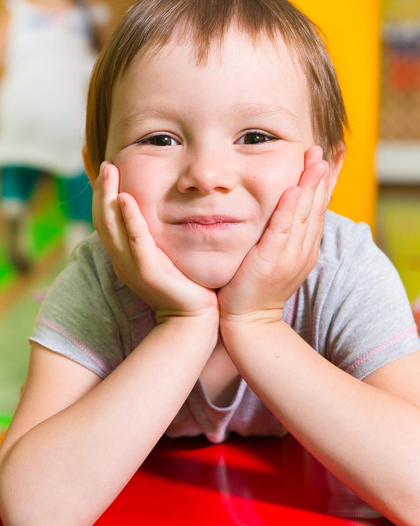 A preschooler resting his chin on his hands and smiling at the camera