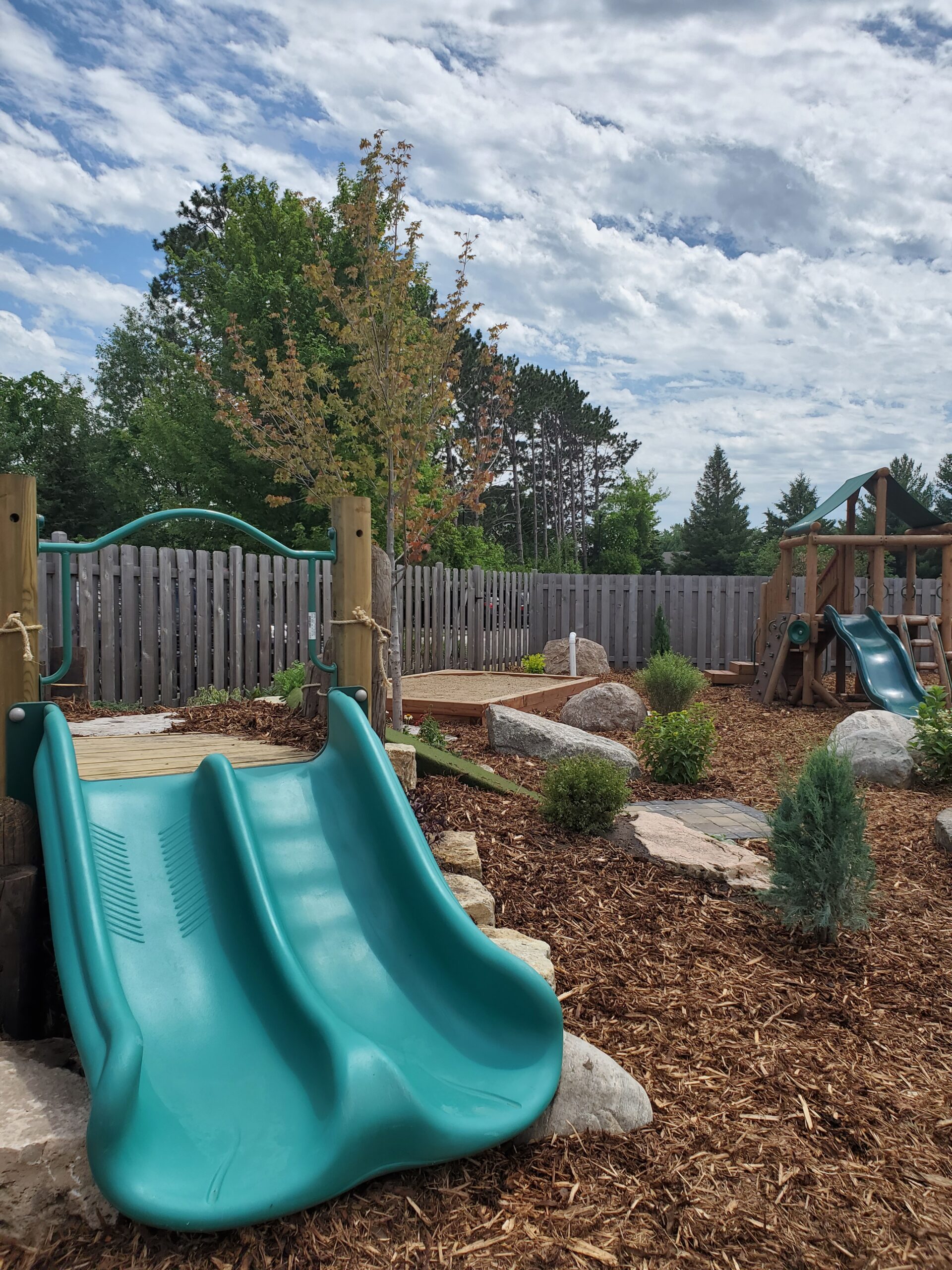 A playground with slides and rocks in the yard.