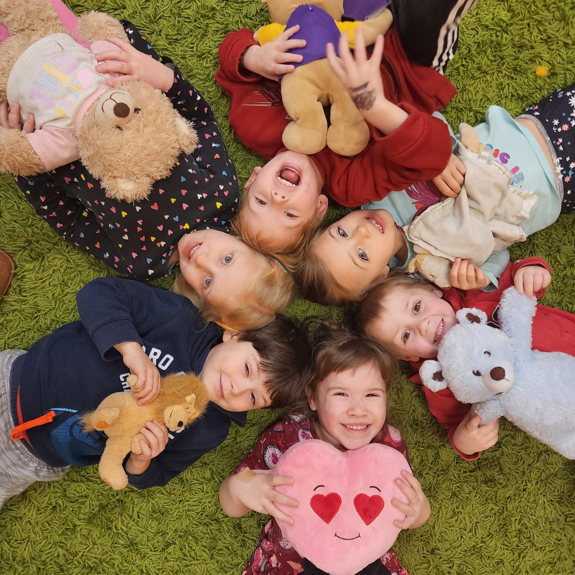 A group of children laying on the ground with stuffed animals.