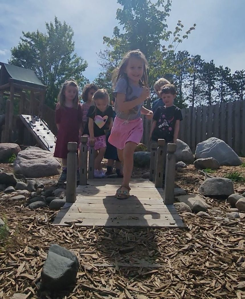 Children crossing the wooden bridge on the natural playground, boulders and wood chips underfoot