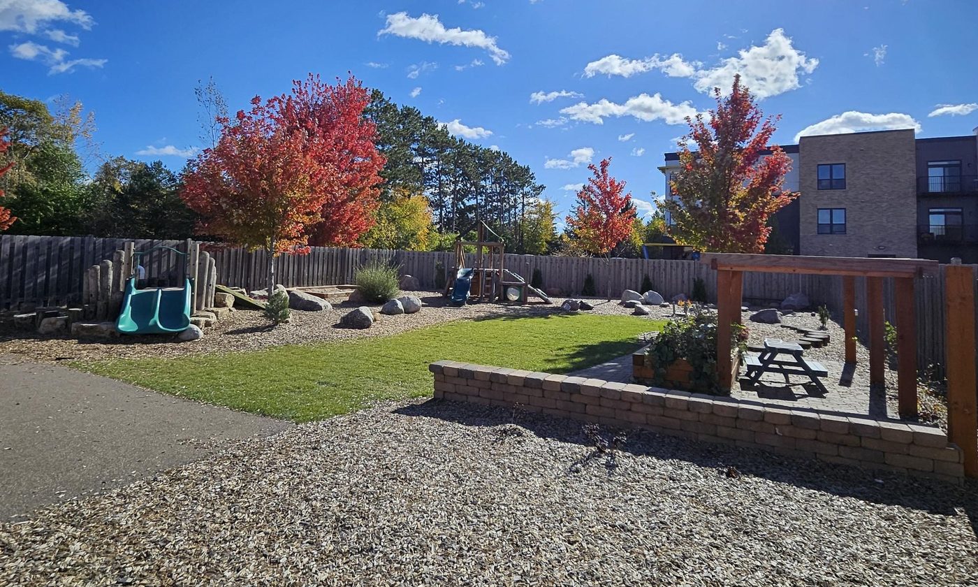 The second playground in fall color: slide, pergola and picnic table among red maples