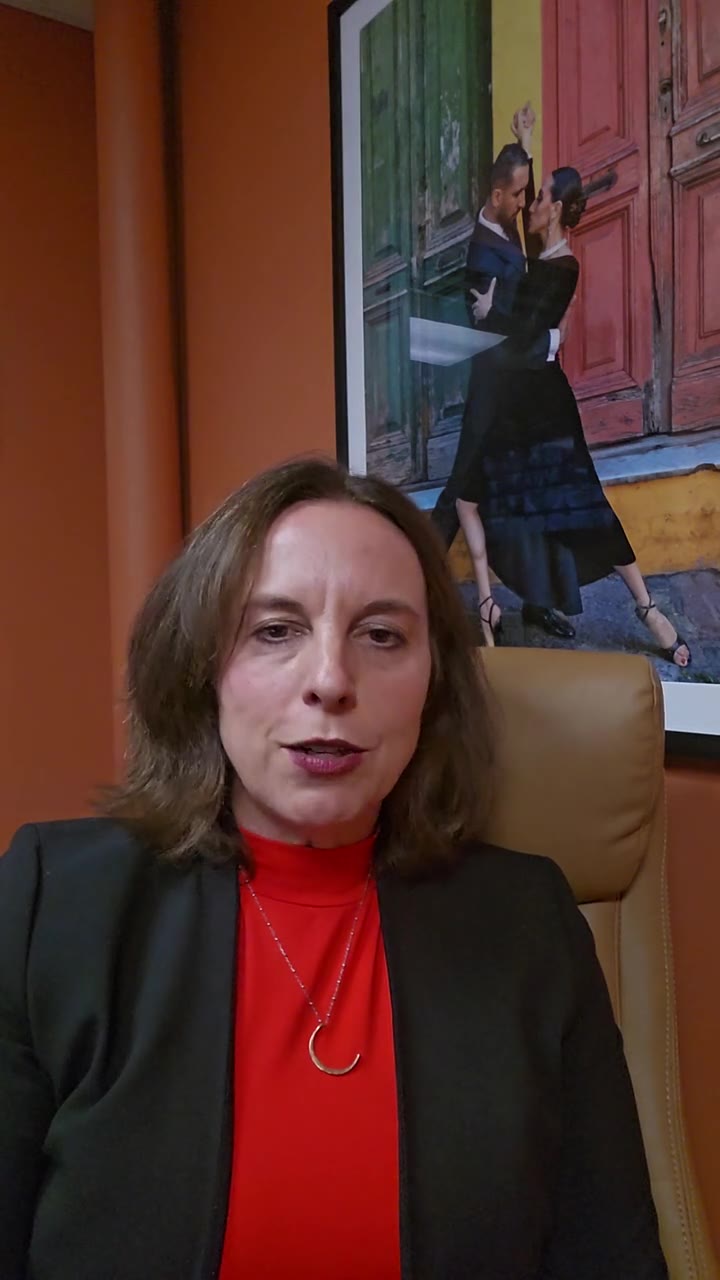 Leah Retamozo seated in her office in front of an orange wall, talking to camera about how to enroll