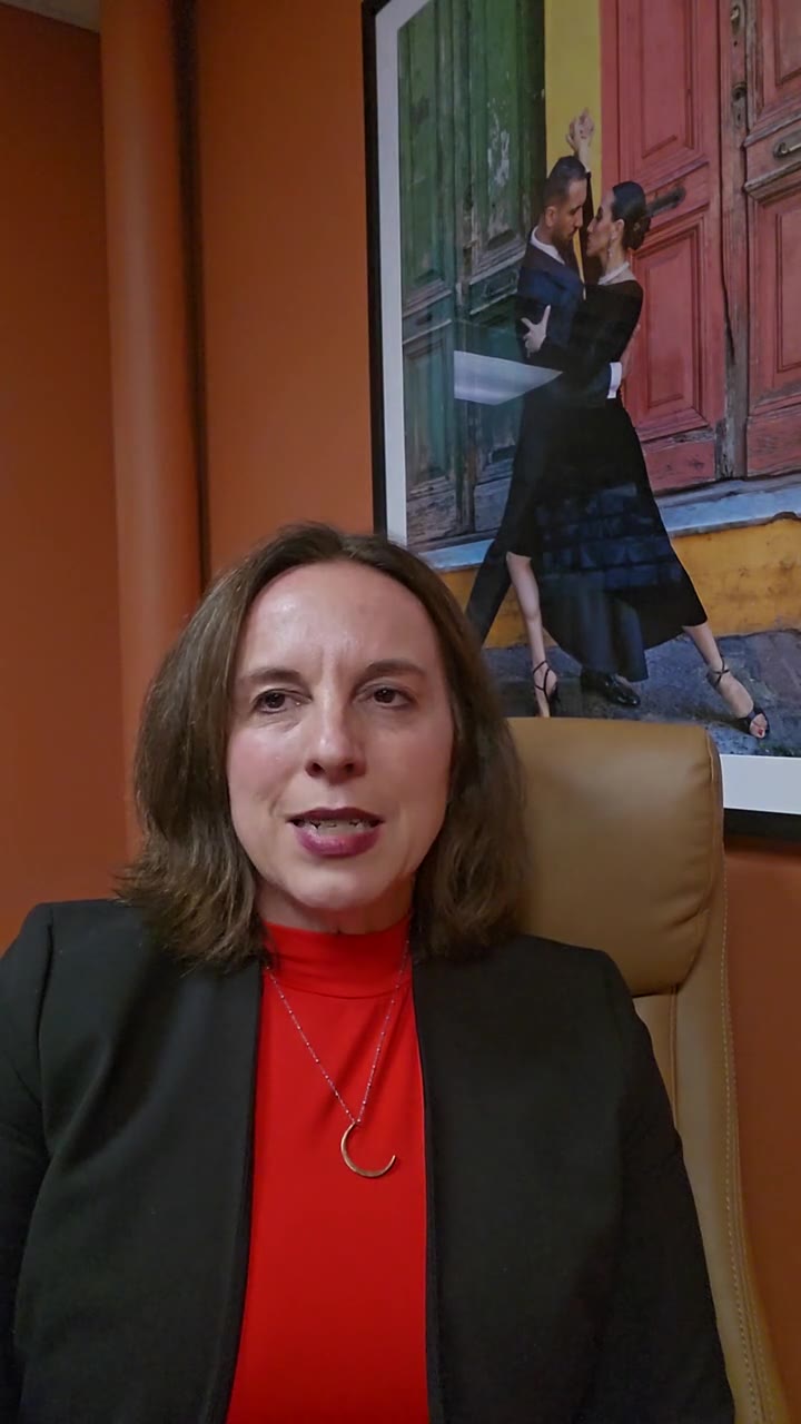 Leah Retamozo seated in her office in front of an orange wall, talking to camera about the program